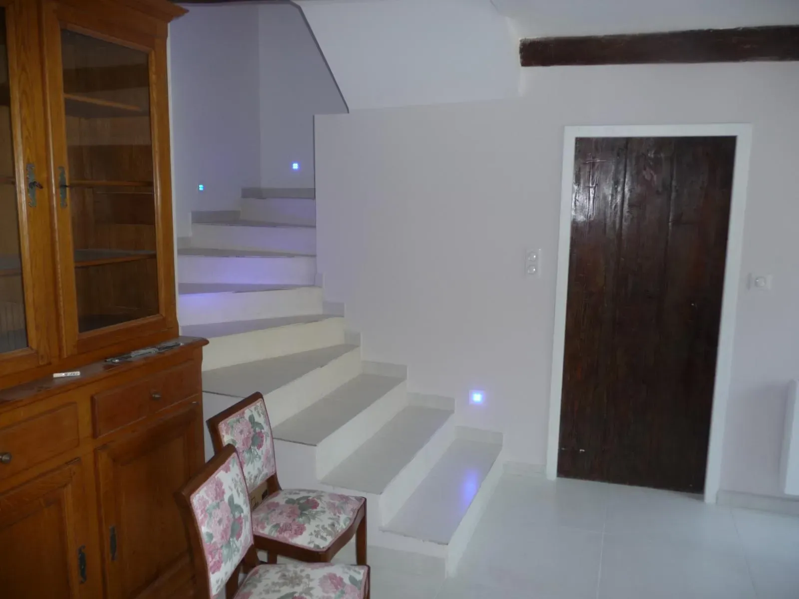 Escalier blanc à éclairage intégré dans les marches, poutre apparente et porte ancienne en bois sombre