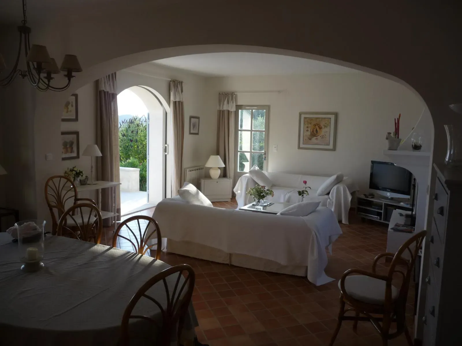 Séjour vu à travers une large arche, sol en tomettes, porte-fenêtre cintrée ouverte sur le jardin