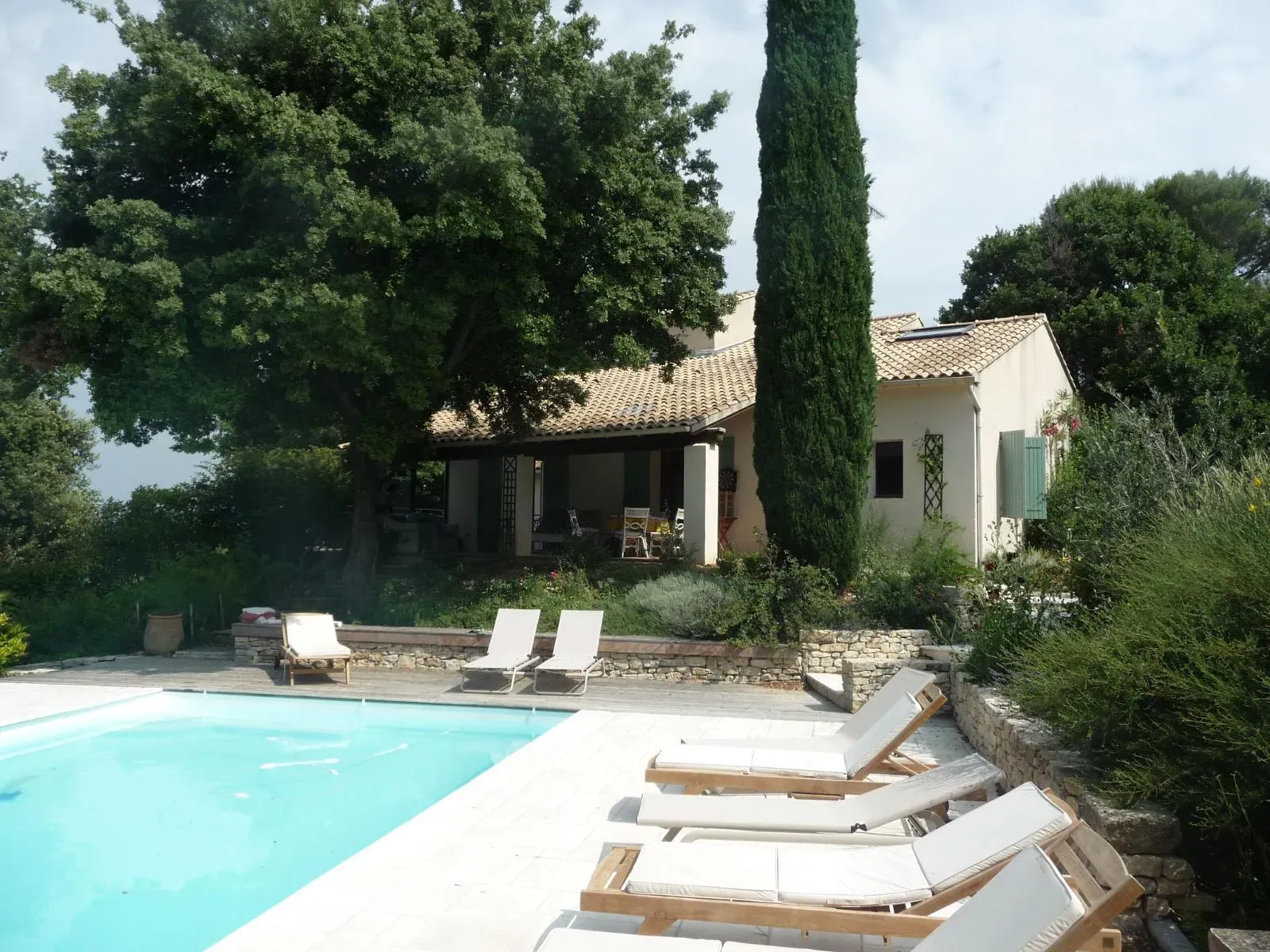 Maison sous un grand chêne et un cyprès, terrasse couverte, piscine bordée de dallage et de murets en pierre