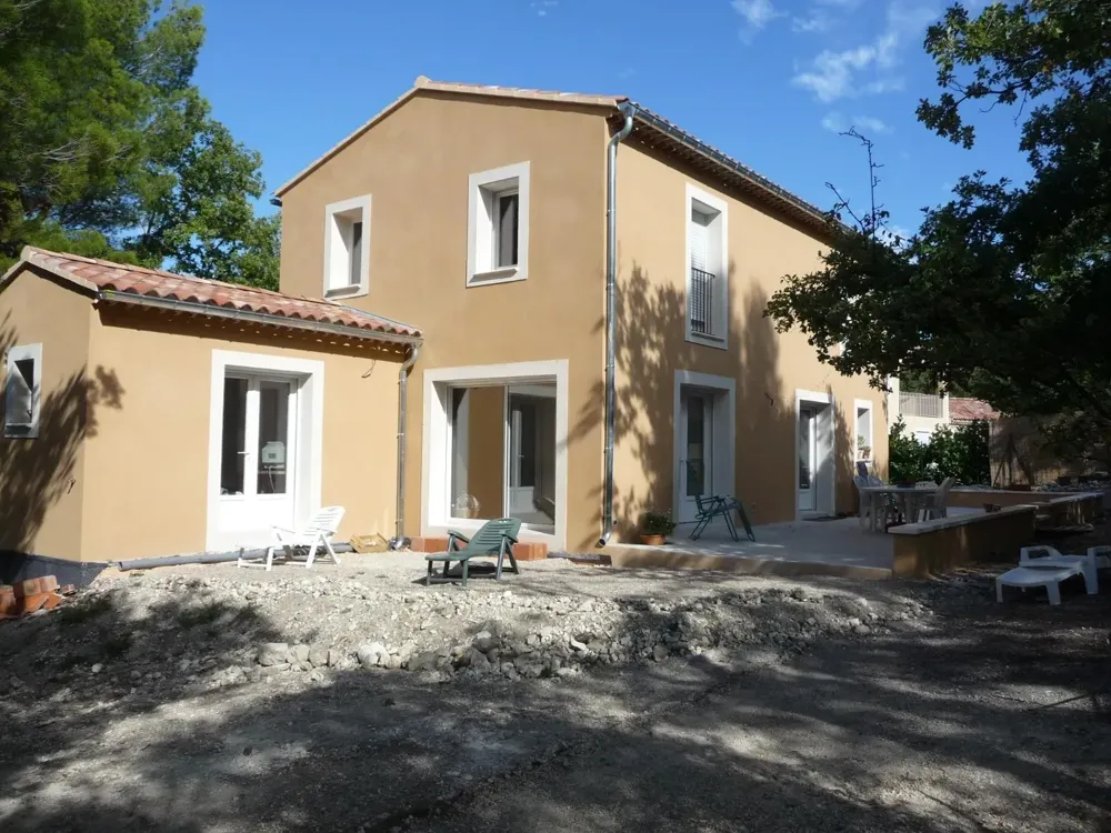 Maison à étage aux façades ocre et encadrements blancs, terrain encore en gravats devant la terrasse